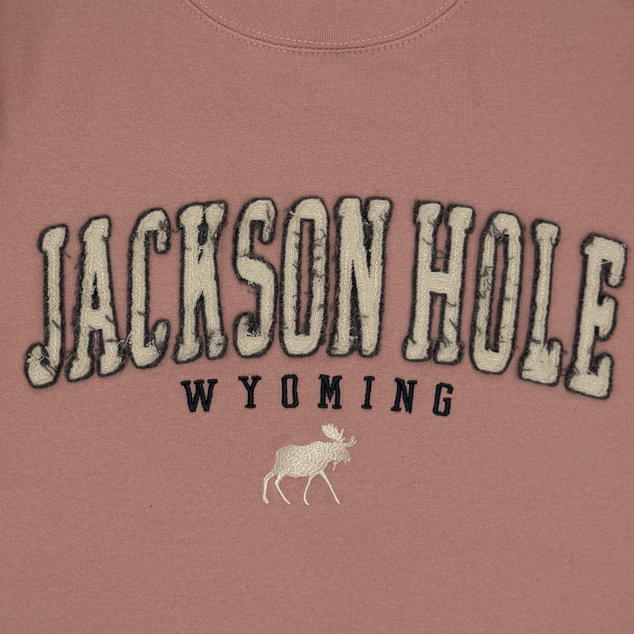 Pink sweatshirt with 'Jackson Hole Wyoming' text on a white background